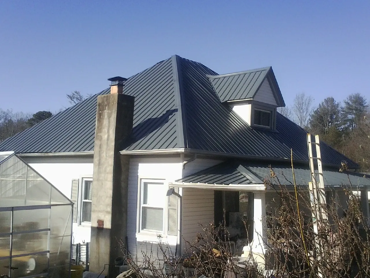 Dark blue standing seam metal roof on a white farmhouse with dormer — Slate & Tile Roof Repair by Roofing Brothers in Dunlap
