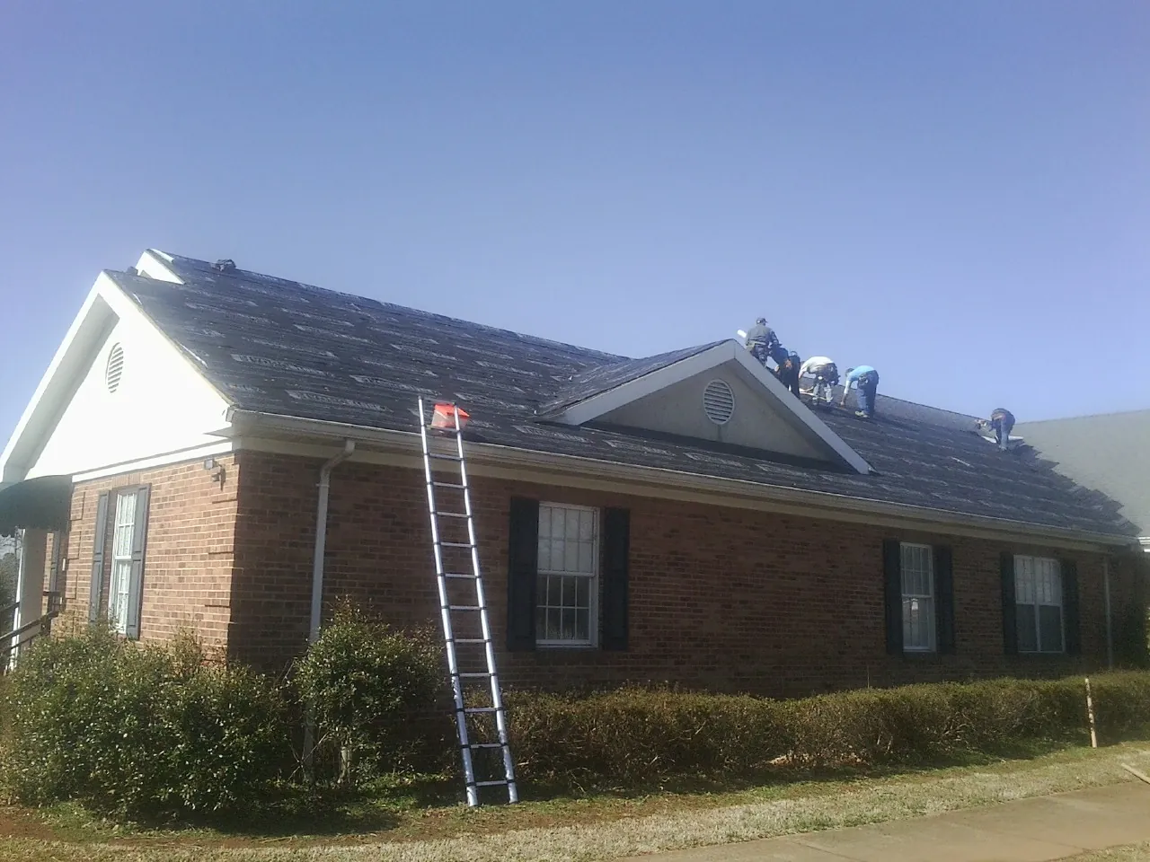 Crew tearing shingles off a brick ranch roof with a ladder set — Emergency Roof Repair work by our crew in Dunlap