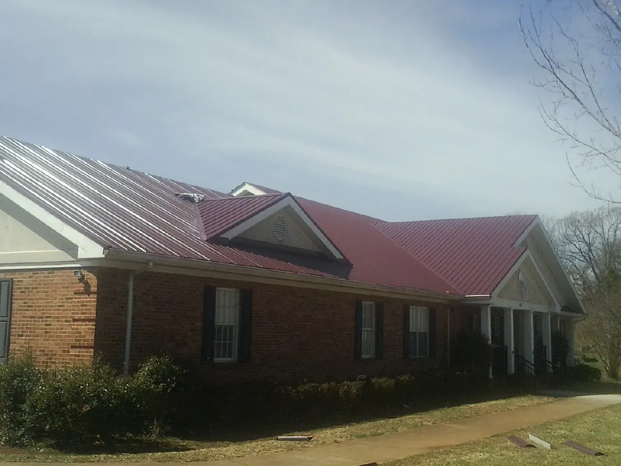 Red metal roof with gabled entries on a long brick building, from a Hail Damage Roof Repair job in Dunlap