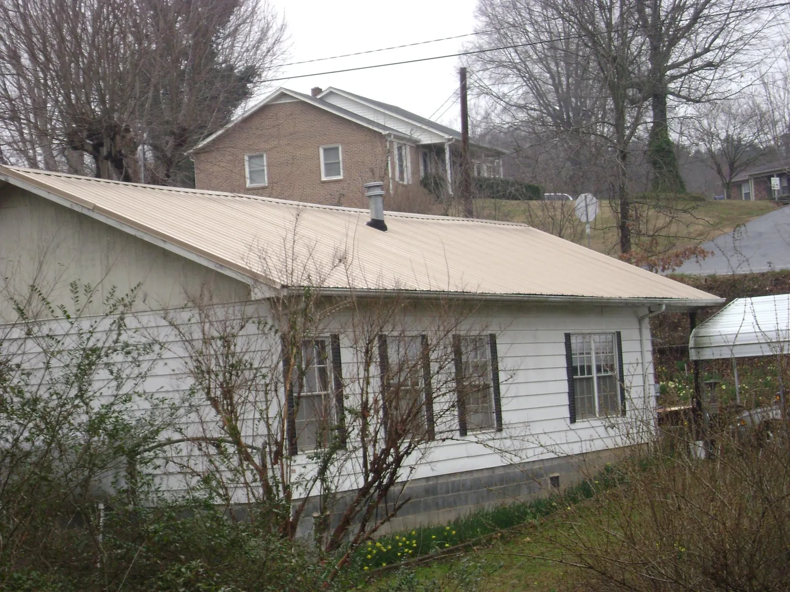 Tan metal roof on a white sided house set into a hillside — Commercial Roofing by Roofing Brothers in Dunlap